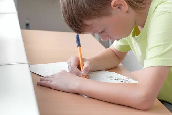 Menino da escola aprende a escrever cartas sentadas à mesa. Fazer trabalhos de casa . — Fotografia de Stock