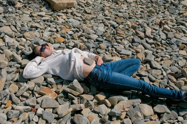 Femme en lunettes de soleil couchée sur une plage de pierre à l'automne. Pierre sur le ventre des filles . — Photo