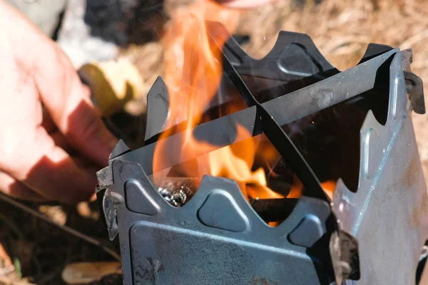 Man inflames metal camp furnace stove on woods outdoors. Mens hands close-up. Top view. — Stock Photo, Image