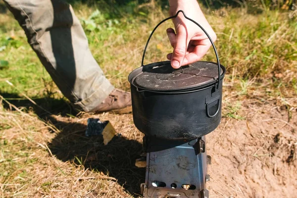 El hombre abre una olla en una estufa de horno de campamento de metal en los bosques al aire libre. Primer plano de la mano . — Foto de Stock