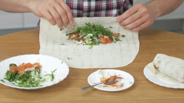 El hombre está cocinando shawarma en la mesa de la cocina en casa. Pita, verduras y cebolla verde con salsa y mayonesa. Primer plano de las manos . — Vídeos de Stock