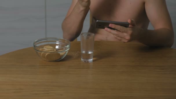 Junger Mann, der nachts in der Küche Kekse isst und aufs Telefon schaut. Schlaflosigkeit und Angst. Übermäßiges Essen. Hände aus nächster Nähe. — Stockvideo