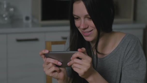 Krásná mladá žena kradmo hraje hry na mobilním telefonu v kuchyni v noci. — Stock video