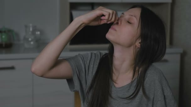 Άρρωστος νεαρή γυναίκα στάζει σταγόνα ρινική στη μύτη στην κουζίνα το βράδυ. Θεραπεία της ρινίτιδας στο σπίτι. — Αρχείο Βίντεο