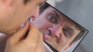 Genç adam evde aynanın önünde cımbız ile onun kıllar burun kendiniyoluyor.