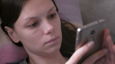 Üzgün kadın kanepede yatan ve cep telefonu, bir şey okuma. Yakın çekim yüz.