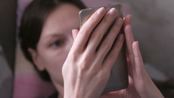 Uma mulher deitada no sofá e a ler alguma coisa no telemóvel. Close-up mãos com telefone . — Vídeo de Stock
