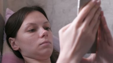 Gergin kadın kanepede yatan ve cep telefonu, bir şey okuma. Yakın çekim yüz.