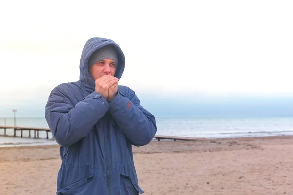 Ο άνθρωπος σε ένα σακάκι από την θάλασσα παγωμένο ζεσταίνει τα χέρια και αναμονή για κάποιον. — Φωτογραφία Αρχείου