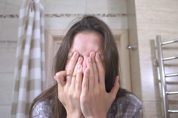 Woman covers her face with her hands standing in the bathroom. — Stock Photo, Image