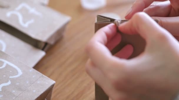 Una donna fa il calendario dell'avvento di Natale per i bambini. Scrive un numero sulla borsa con pennello e vernice bianca. Mani in primo piano . — Video Stock