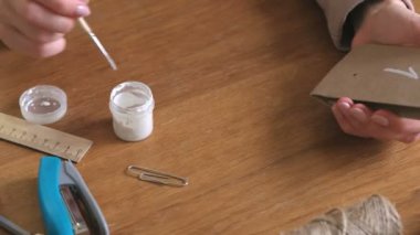 Kadın, çocuklar için Noel varış takvim yapar. Birkaç çanta üzerinde fırça ve beyaz boya ile yazar. Yakın çekim yakışıklı.