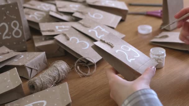 La mujer hace el calendario de Adviento de Navidad para los niños. Escribe un número en la bolsa por pincel y pintura blanca. Primer plano de las manos . — Vídeos de Stock