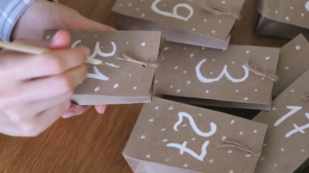 女人为孩子们制作圣诞年历。用刷子和白色油漆在袋子上写一个数字。特写镜头. — 图库视频影像
