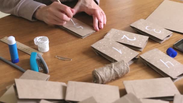 Woman makes christmas advent calendar for kids. Writes a number on the bag by brush and white paint. Close-up hands. — Stock Video