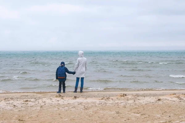 Maman et son fils marchent sur la plage de sable marin en hiver, vue arrière. Belle vue sur la tempête de sable et de neige sur la plage . — Photo