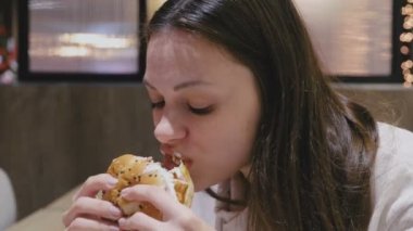 Kafede hamburger zevkle ve zevk ile yemek kadın. Yan görünüm.
