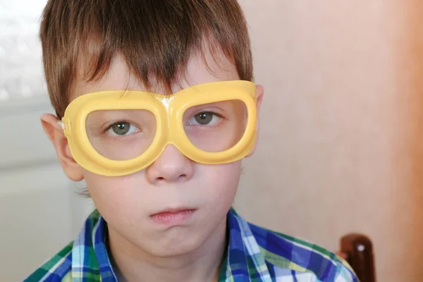 Seriosly boy in safety yellow goggles sitting at the table and looking at camera. Experiments on chemistry at home. — Stock Photo, Image