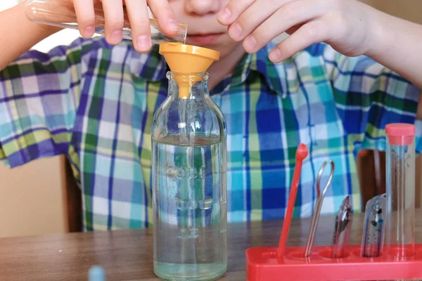 Эксперименты по химии дома. Крупным планом мальчиков руки наливали воду из трубки в бутылку через воронку . — стоковое фото