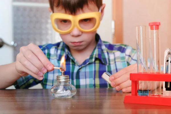 Experimenten op chemie thuis. Jongen stelt de brandende alcohol lamp in vuur en vlam met een wedstrijd. — Stockfoto