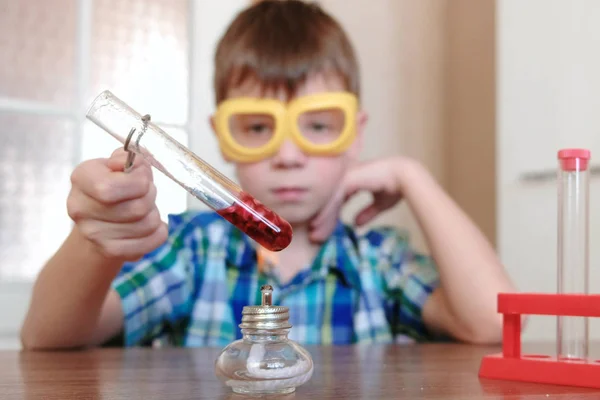 Experimentos de química en casa. Chico calienta el tubo de ensayo con líquido rojo en la lámpara de alcohol ardiente. Desenfoque . —  Fotos de Stock