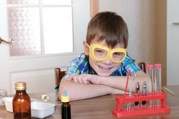 Kísérletek, a kémia otthon. Kockás ing mosolygó fiú ül az asztalnál, és megy a gyakorlat kémia kísérletek. — Stock Fotó