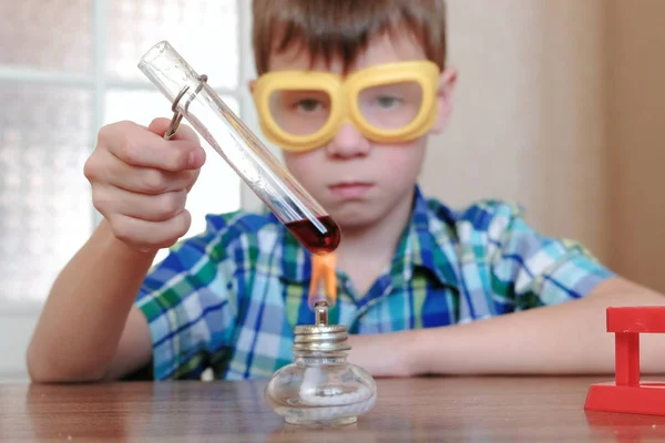 Experimentos de química en casa. Chico calienta el tubo de ensayo con líquido rojo en la lámpara de alcohol ardiente . — Foto de Stock