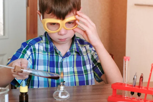 家庭で化学の実験。少年は、アルコール ランプの燃焼の赤い液体で試験管を加熱します。液体の沸騰. — ストック写真