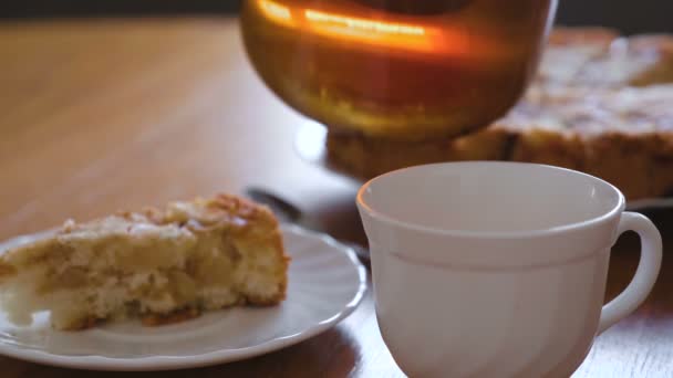 Nahaufnahme Frauenhände gießt einen Tee auf eine Tasse aus Teekanne. Scheibe eines hausgemachten Apfelkuchens auf Untertasse. — Stockvideo