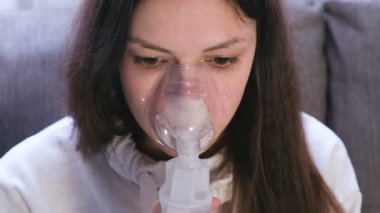 Nebulizatör ve astım tedavisi için kullanın. Genç kadın kanepede oturan inhaler maskesi aracılığıyla teneffüs edilmesi. Yakın çekim yüz.