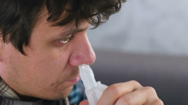 Sjuk man andas in genom inhalatorn munstycke för näsan. Närbild ansikte, sidovy. Använda nebulisatorn och inhalator för behandling. — Stockvideo