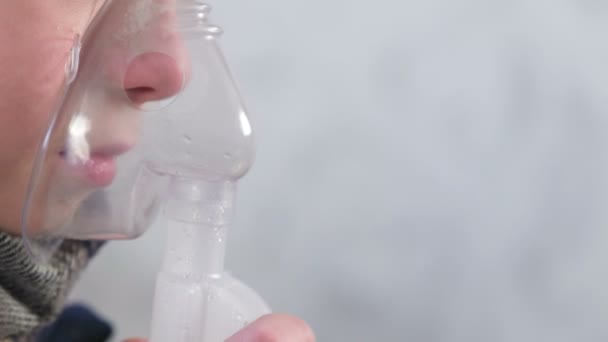 Больной мальчик вдыхает через маску ингалятора, нос и губы вид сбоку. Использование ингалятора и распылителя для лечения . — стоковое видео
