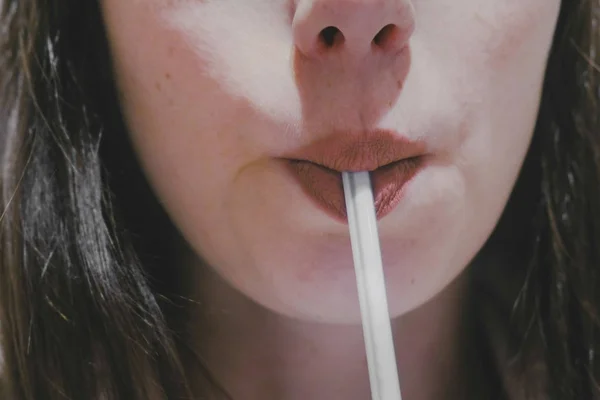 Hermosa mujer está bebiendo una bebida de un tubo, labios de cerca . — Foto de Stock