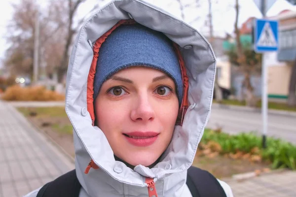 Woman in hat and hood looking into the camera and smiling.