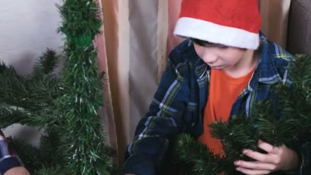 Menino feliz com a mãe em chapéu de Natal instalar árvore de Natal em casa. Prepare-se para o Natal . — Vídeo de Stock