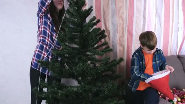 Moeder en zoon in Kerstmis hoeden versieren kerstboom met kralen en ballen. — Stockvideo