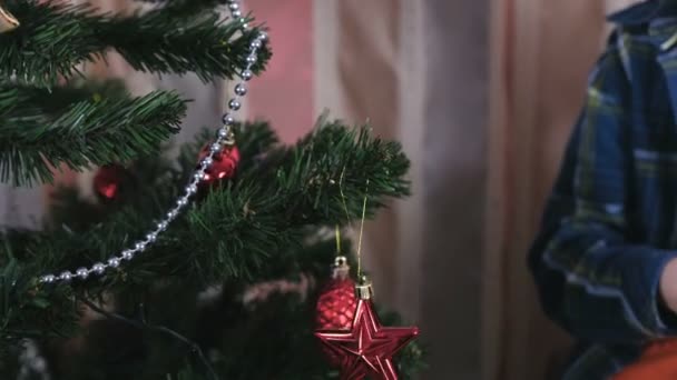 Mutter und Sohn in Weihnachtsmützen schmücken den Weihnachtsbaum mit Perlen und Kugeln. Hände aus nächster Nähe. — Stockvideo