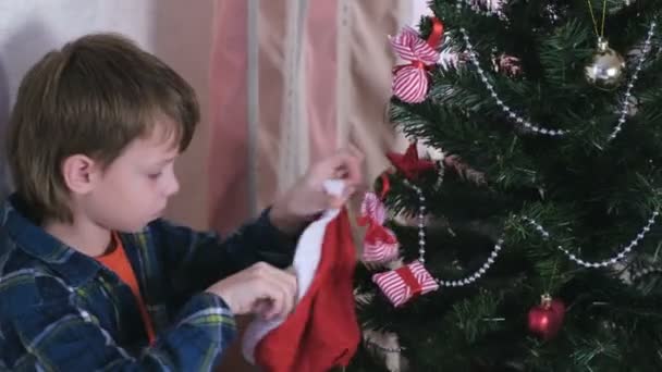 Boy take christmas decorations from christmas hat and decorates christmas tree. — Stock Video