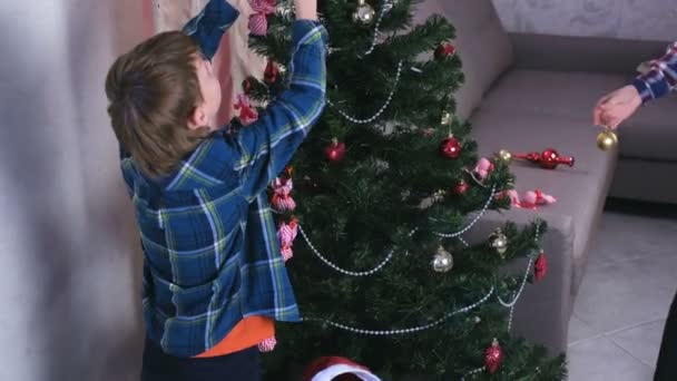 Mãe e filho em chapéus de Natal decorar árvore de Natal com contas e bolas . — Vídeo de Stock