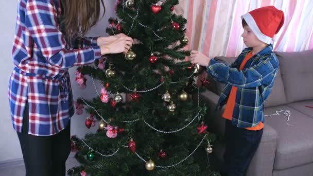 Μαμά και γιος στο Χριστούγεννα καπέλα διακοσμήσετε το χριστουγεννιάτικο δέντρο με χάντρες και μπάλες στο σπίτι. — Αρχείο Βίντεο