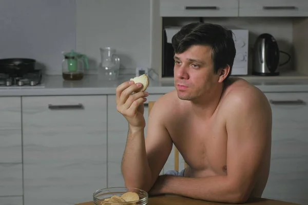Νεαρός άνδρας τρώει μπισκότα στην κουζίνα το βράδυ. Αϋπνία και το άγχος. Υπερβολικό φαγητό. — Φωτογραφία Αρχείου