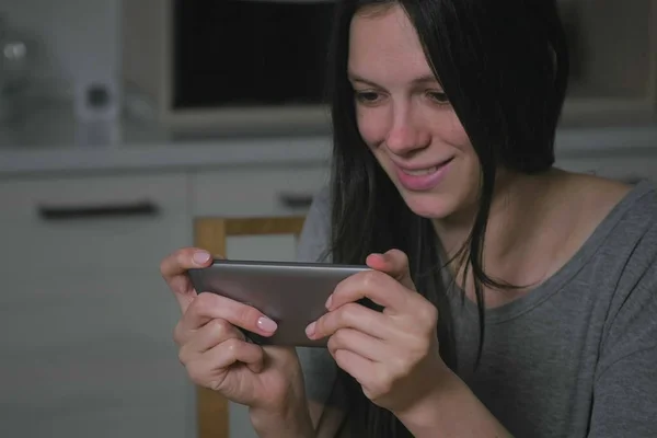 Красивая молодая женщина украдкой играет в игры на мобильном телефоне на кухне ночью . — стоковое фото