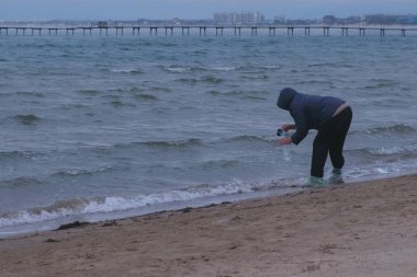 Yaşlı kadın gezgin deniz bir şişe su kumlu bir plaj üzerinde duran kazanıyor. Deniz kıyısı sonbaharda. Deniz Hediyelik eşya.