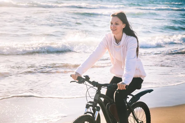Hermosa joven monta una bicicleta a lo largo del mar en una playa de arena . —  Fotos de Stock