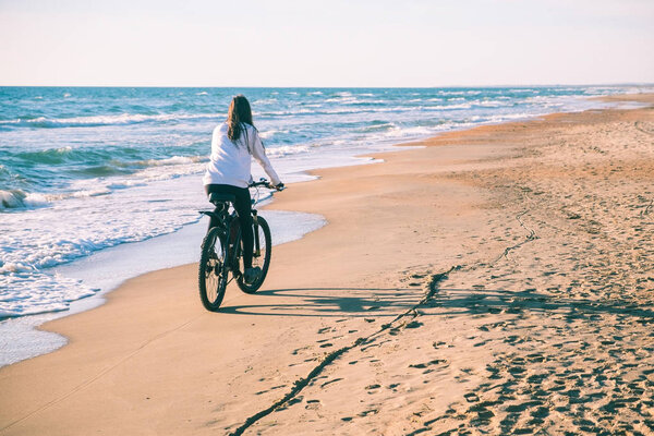 Woman rides a Bicycle along the sea on a sandy beach. Back view.