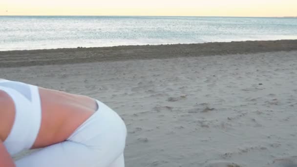 Genç kadın kumsalda güneş doğarken germe yoga yapıyor. — Stok video