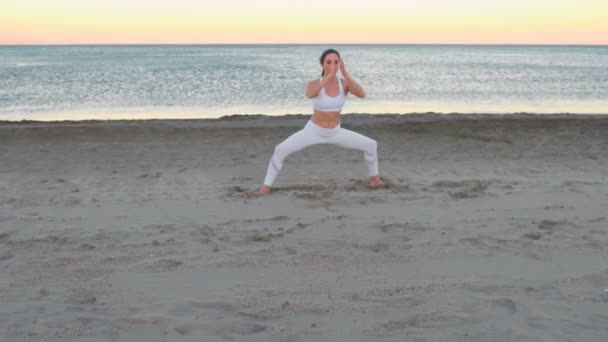 Young woman doing yoga sitting in front splits on the sandy beach at sunrise. — Stock Video