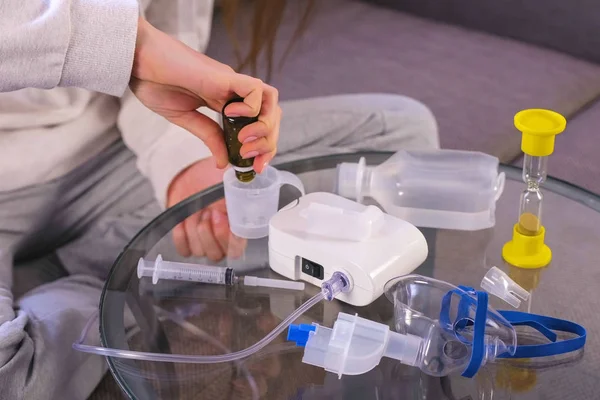 Woman puts medicine in the part of the inhaler. Hands close-up. Medicine for inhalation and nebulizer on the glass table.