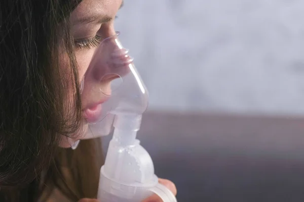 Use nebulizador e inalador para o tratamento. Mulher jovem inalando através da máscara do inalador, close-up da face, vista lateral . — Fotografia de Stock