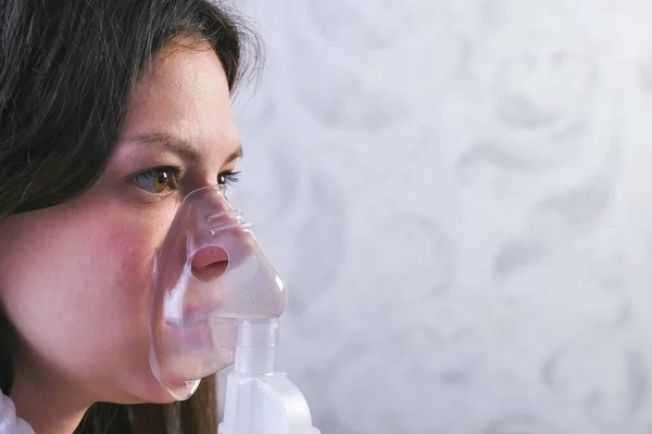 Use nebulizador e inalador para o tratamento. Mulher jovem inalando através da máscara do inalador, close-up da face, vista lateral . — Fotografia de Stock